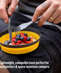 Person using Frontier Ultralight Collapsible Bowl Large 30 Fl Oz Puffins Bill Orange with fruit salad outdoors.