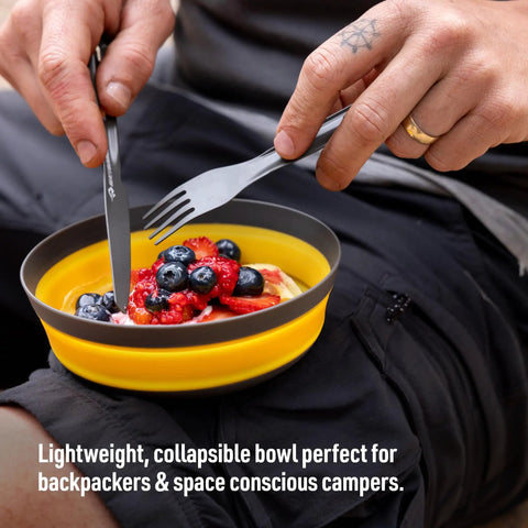 Person using Frontier Ultralight Collapsible Bowl Large 30 Fl Oz Puffins Bill Orange with fruit salad outdoors.