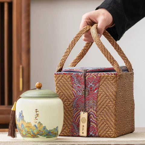 Top Shelf Ceramic Tea Tin With Woven Rattan Travel Case, Stunning Mountain Landscape Design, Go To Stash Jar For Loose Leaf Tea Or Specialty Coffee Beans In Slate Blue beside a wicker pouch.