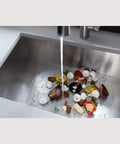 Continuous Feed Garbage Disposal 1/2 HP with 2600+ RPM grinding vegetable scraps and cooked meat under running water in a sink