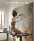 Yihayo 55 Inch L Shaped Electric Standing Desk in use, supporting 154lbs, with artist painting on top.