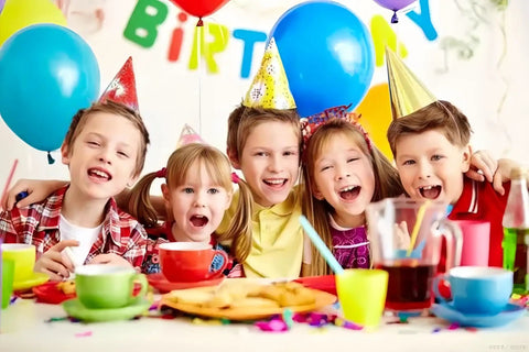 Group of children wearing party hats celebrating at a colorful birthday party with balloons and festive decorations.