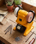 Slick Cordless Mini Bench Grinder With 70mm Wheel And 5500 RPM For Quick Sharpening And Polishing Jobs Around The Shop No Wire Hassle Just Drop Your 18V Pack And Roll on a wooden workbench with tools.