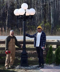 Two people standing beside 9.5 Ft Five Arm Victorian Outdoor Post Light in Black Finish, shown in a forested driveway setting.