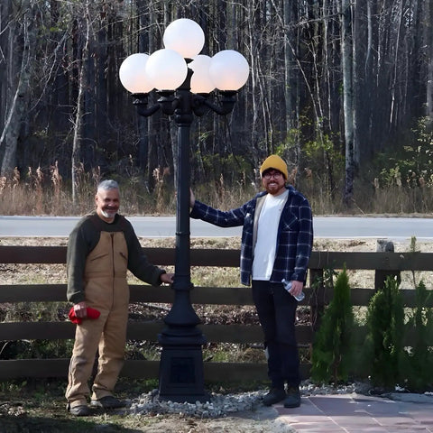 Two people standing beside 9.5 Ft Five Arm Victorian Outdoor Post Light in Black Finish, shown in a forested driveway setting.
