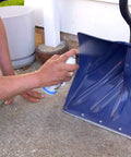 Person applying 6-16-TDL Advanced Dry Lube With Teflon 9.3 Oz Pack Of 6 to a blue snow shovel resting on concrete