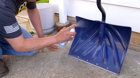 Person applying 6-16-TDL Advanced Dry Lube With Teflon 9.3 Oz Pack Of 6 to a blue snow shovel resting on concrete