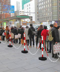 Nine Pack Traffic Delineator Cones With Base Set Red Plastic Safety Cones For Parking Lot Use Includes Six Point Six Feet Link Chain And S Hooks Stanchion Style Barriers For Easy Area Demarcation in use on a city sidewalk.