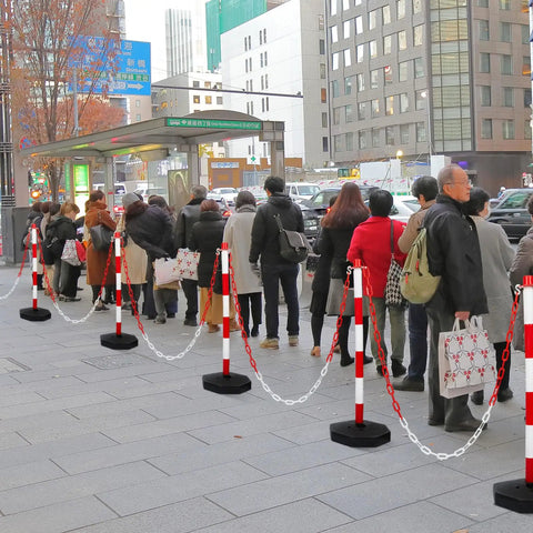 Nine Pack Traffic Delineator Cones With Base Set Red Plastic Safety Cones For Parking Lot Use Includes Six Point Six Feet Link Chain And S Hooks Stanchion Style Barriers For Easy Area Demarcation in use on a city sidewalk.