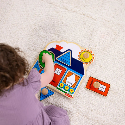 Toddler playing with First Shapes Jumbo Knob Puzzle For Toddlers With Wooden Peg Pieces on a cream carpet, showing house puzzle shapes.