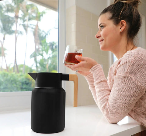 Woman enjoying a drink beside a 50 Oz Stainless Steel Thermal Coffee Carafe Insulated Vacuum Double Walled Beverage Dispenser With Tea Infuser And Strainer For Hot Or Cold Drinks Keeps Your Brew Hot Or Cold For Hours