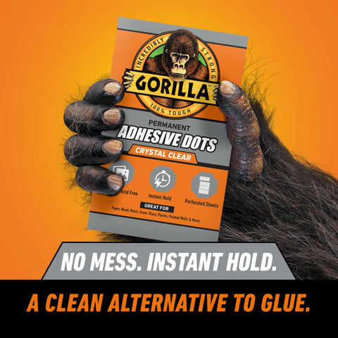 Close-up of a gorilla hand holding a pack of crystal clear adhesive dots, promotional text about no mess and instant hold visible.