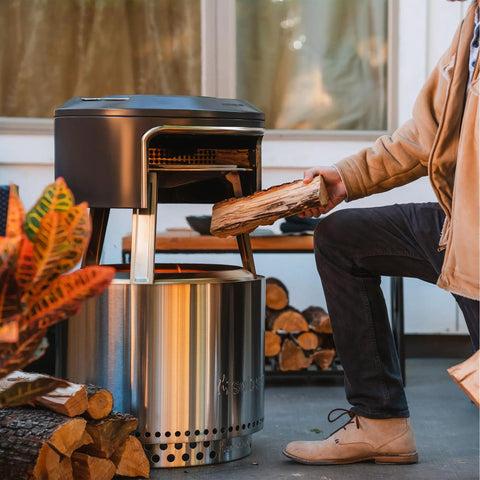 Bonfire Pi Fire Pizza Oven Accessory For Fire Pit With Cordierite Pizza Stone And Carry Case Wood Burning Assembly Stainless Steel Build Elevate Pizza Nights Grillin On The Pit in use with wood being added to fire pit.
