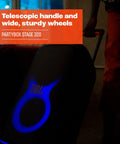 Stage 320 Portable Party Speaker with telescopic handle and wide wheels, glowing blue light show for outdoor events.