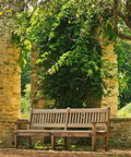 Wooden bench set against stone structure, surrounded by lush greenery in a serene garden setting.