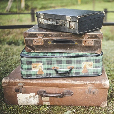 Stack of four vintage suitcases in various colors and materials outdoors on grass, showcasing retro travel style.