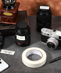 Console Labeling Tape 1 Inch Wide 54.7 Yard Roll Clean Writable Flatback Paper White Adhesive Tape Removable No Residue shown with camera lenses and notes.