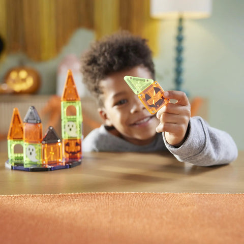 Child smiling while holding neon block, building a mini haunted house with 24 Piece Halloween Magnetic Building Tiles For Kids.