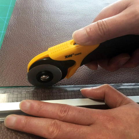 Hands using 45mm Rotary Cutter And Precision Knife Set For Art Quilting And Crafting With 12 Bonus Blades Pro Grade Ergonomic Aluminum Handle Anti Slip Grip Safe Retracting Blade For Precise Clean Cuts on fabric with ruler.
