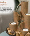 Indoor Tabletop Tiered Water Fountain With 3 Candles, 11 Inch Brown, placed on a table surrounded by rocks, creating a cozy ambiance