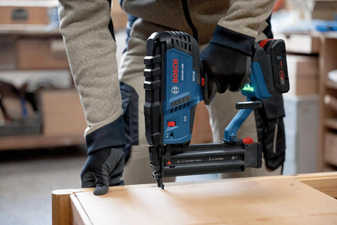 Gutsy 18 Volt Brushless Cordless Brad Nailer Kicks Out 2,000 Nails Per Charge With One Thumb Safety Trigger Zero Hassle Jam Clearance And Built In Dual Lamps For Low Light Jobs No Battery Or Charger Included, being used to nail wood.