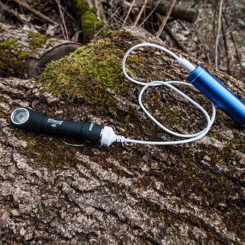Wizard Pro V3 XHP50 Warm USB Magnetic Headlamp with 2300 Lumens on mossy log connected to blue USB charger