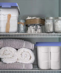 Kick Ass 32 Quart Clear Plastic Stackable Storage Bins With Blue Latching Lids organizing towels on shelf in bathroom storage.