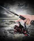 Angler holding Beast Mode Baitfeeder III Spinning Fishing Reel Size 6000 in action on rocky shoreline, showcasing design and grip.