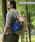 Man outdoors carrying a portable hammock bag with the Camping Hammock With Mosquito Net For Outdoor Travel Portable Lightweight Parachute Nylon Hammock With Tree Straps And D Shape Carabiners Breathable Mesh Net Backpacking Ready For Beach Backyard Patio Hiking