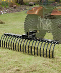 Tow Behind Landscape Rake 60 Inch Dethatcher with 21 Steel Coil Tines attached to tractor for yard cleanup.