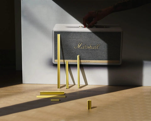 Yellow bars arranged on floor in front of a white and black speaker with a hand reaching towards it, creating a shadowed visual.