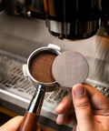 Close-up of 54mm stainless steel bottomless espresso portafilter with rosewood handle and puck screen