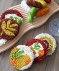 Punch Needle Coaster Kit For Beginners And Adults With Patterns Tools Yarns Hoop Adhesives Coaster Holder And Easy To Follow Instructions featuring colorful plant-themed yarn coasters on a wooden board.