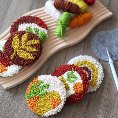Punch Needle Coaster Kit For Beginners And Adults With Patterns Tools Yarns Hoop Adhesives Coaster Holder And Easy To Follow Instructions featuring colorful plant-themed yarn coasters on a wooden board.