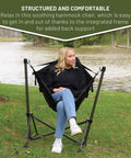 Person sitting in Portable Hammock Camping Chair With Stand by a lake, stainless steel frame, outdoor setting