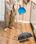 Person using Dark Grey Angle Floor Broom With Long Stainless Steel Handle And Dense Stiff Bristles to clean kitchen floor.