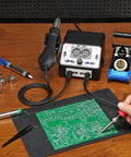 Person using 2 In 1 Soldering Iron Station And Hot Air Rework System With LCD Display, PID Temp Control, and solder wire on circuit board.