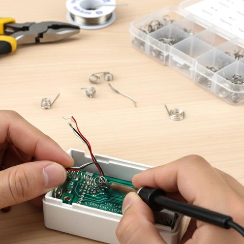 Soldering AA coil with Dope 50 Pack Battery Spring Replacement Set for electronics repair, coils visible, tools on desk.