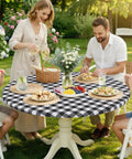 Family dining outdoors on a round table with a black and white buffalo plaid tablecloth, matching the Round Picnic Tablecloth With Elastic Edges Waterproof Fitted Vinyl Cover For 36 to 44 Inch Tables Flannel Back Buffalo Plaid Black And White No Slip Windproof Outdoor Dining.