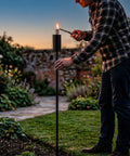Person lighting a 55 Inch Outdoor Oil Torch Lamps Four Pack Rustproof Stainless Steel Citronella Torches at dusk in a garden