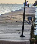 Fishing rod resting on a wooden dock over water with two people sitting in chairs in the background