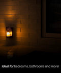 Decorative LED Night Light with Plug-In Dusk-To-Dawn Sensor in Warm White Brushed Nickel Finish for Living Room Bedroom Nursery Kitchen or Bathroom, glowing softly on tiled wall.