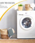 Front view of a white front-loading washing machine in a laundry room with wicker basket, towels, and a potted plant.