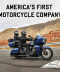 Two people riding a blue Indian Motorcycle on a highway in a desert landscape.