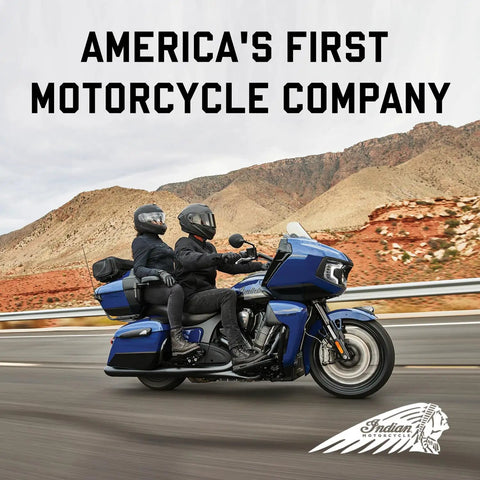 Two riders on a blue Indian motorcycle traveling on a desert highway with text 'America's First Motorcycle Company' above.