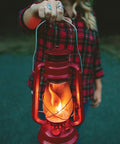 Person holding 12 Inch Hurricane Lantern With Durable Red Finish For Camping And Emergencies glowing brightly in the evening.