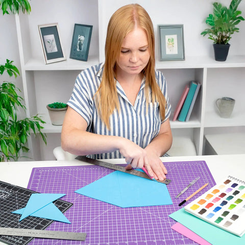 Person using Heavy Duty Stainless Steel Ruler 24 Inch With Cork Backing on a crafting table with colored paper and tools