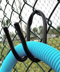 6 Pack Adjustable Chain Link Fence Hooks For Hanging Rakes Pool Poles Nets Brushes Skimmers Vacuum Hoses And More On Your Fence Black Built To Take Outdoor Tough Use And Keep Your Yard Neat, shown holding a blue hose on a chain link fence with black hooks.