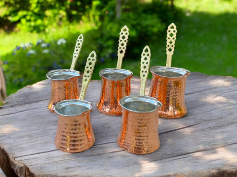 Five handcrafted copper Turkish coffee pots on a wooden table outdoors, part of Handcrafted Copper Turkish Coffee Maker With Five Pots 1000 Watt 110 Volt Barista Level Brew For Turkish Coffee Espresso Tea And More Durable Copper And Stainless Steel Build For Rich Foam And Easy Clean product.