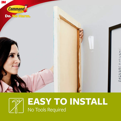 Woman installing Damage Free Canvas Hangers Kit With No Tools Wall Hooks For 18x24 Art Canvases on wall.